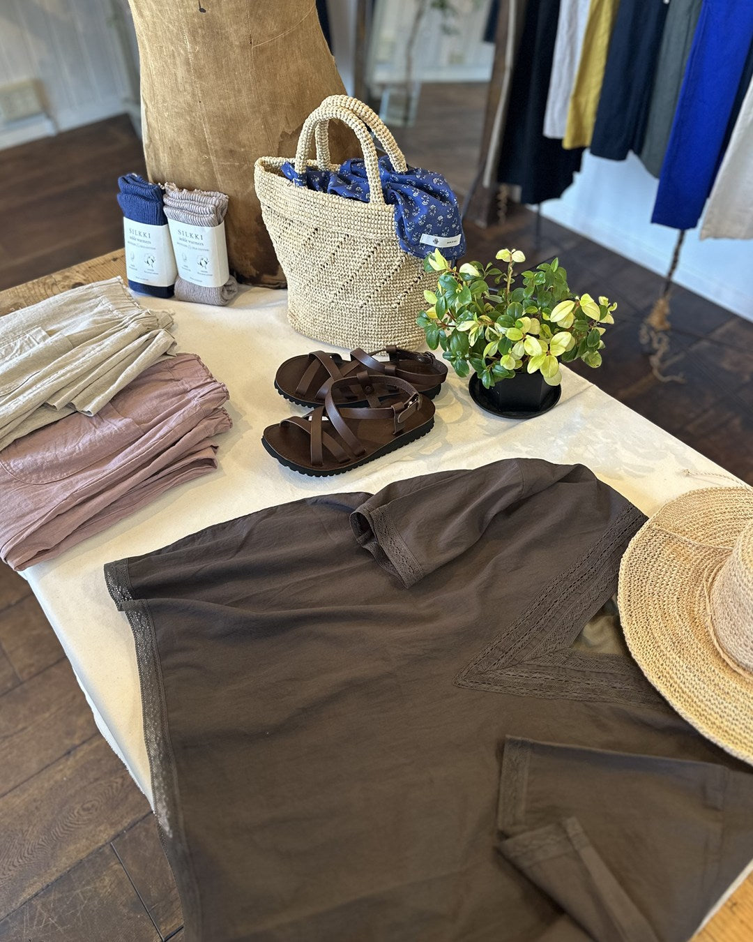 deL’aube店内のテーブルディスプレイ。リネンのパンツ、レザーサンダル、かごバッグ、麦わら帽子、ソックス